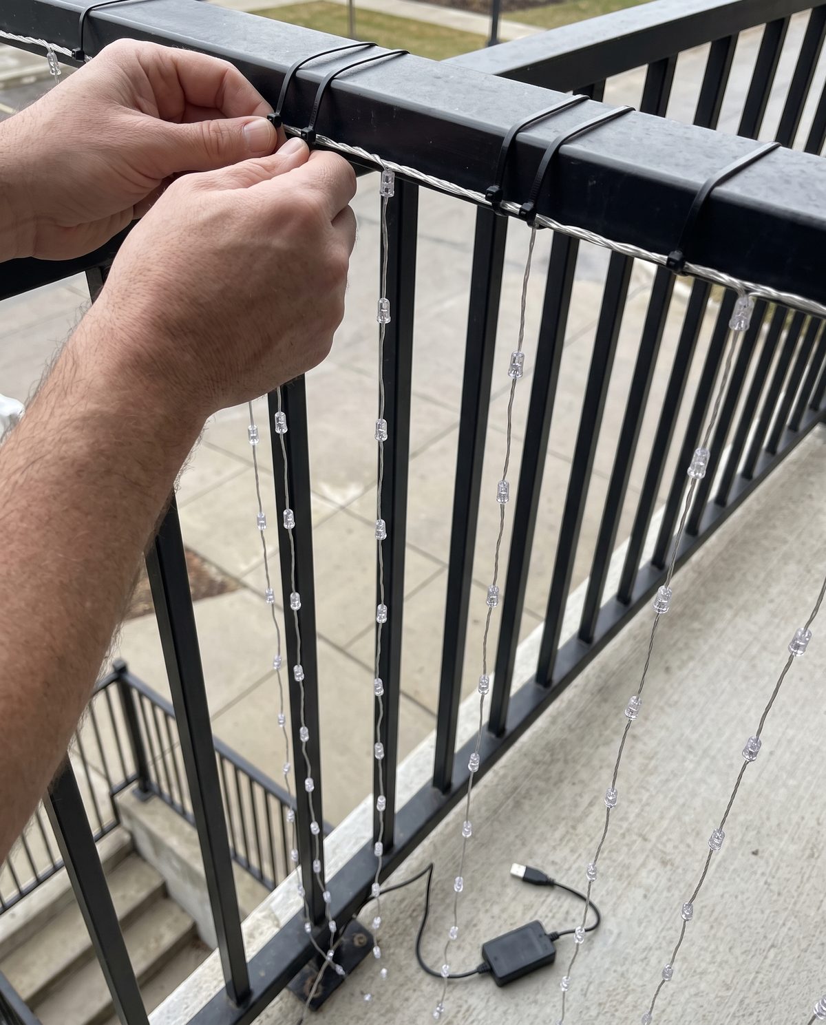 Hands tying the curtain to a balcony railing with cable ties